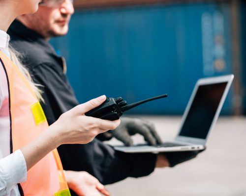 Workers teamwork man woman safety jumpsuit workwear with yellow hardhat use laptop check container cargo shipping warehouse